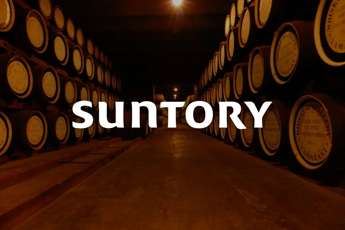 Suntory wordmark over oak whisky casks in the Yamazaki distillery warehouse